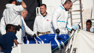 En liksäck med en död migrant bärs i land av den italienska kustbevakningen. En liksäck med en död migrant bärs i land av den italienska kustbevakningen.