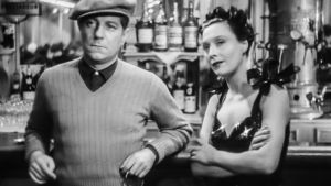Kino klassikko: Varjojen yö. Mies ja nainen istuvat baaritiskillä ja katsovat jonnekin. MV.