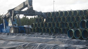 Det är en lönsam affär för Hangö hamn att låta Nord Stream förvara rör i Koverhar (arkivbild). En maskin radar stora rör på varandra.