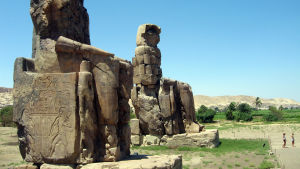Bland annat på det här egyptiska gravtemplet, känt som "Memnons stoder", har romerska turister klottrat graffiti. Två gigantiska egyptiska statyer i ett ökenlandskap.