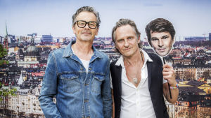 Glenmark, Eriksson, Strömstedt fick en stor hit med en fotbollslåt. Anders Glenmark och Thomas "Orup" Eriksson i närbild med stockholm i bakgrunden. Orup håller i ett paffansikte av Niklas Strömstedt.
