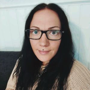 Lena Enlund tycker lönen kunde höjas med tanke på allt närvårdarna utsätts för. Kvinna med mörkt hår och glasögon sitter lutad mot en vägg.