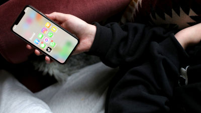 Någon ligger ned i en fåtölj och visar sina telefon. På skärmen står "social" och där finns personens sociala medier-appar.