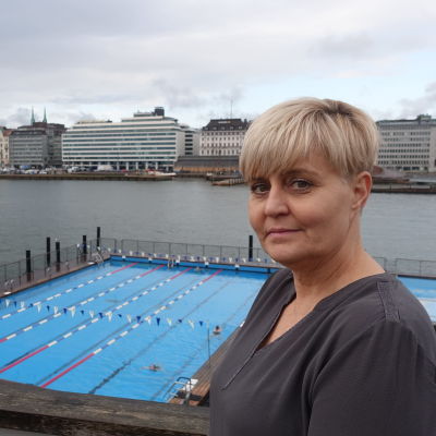 Bodil Ståhl står på uteterassen och i bakgrunden syns bassängerna och husen på Norra kajen