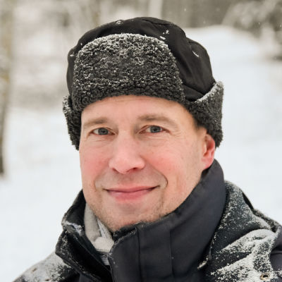 Journalisten och Topeliuspristagaren Peter Buchert ute i ett vintrigt landskap med skog i bakgrunden.