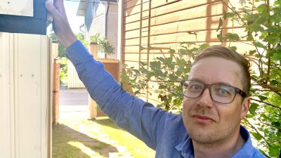 En man med glasögon står med handen mot en halvbyggd träfasad.