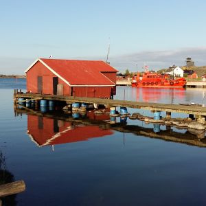 Hamnen i Utö med båthus och en lotskutter som speglas i vattnet.