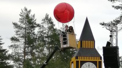 En röd ballong som lfter till väders med folk i korgen, pjäsen Jorden runt på 80 dagar på Raseborgs sommarteater.
