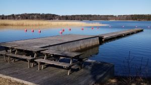 Hotell Merikruunus brygga i Dragsfjärd. En grå träbrygga går ut i vattnet. På bryggan finns bord och bänkar.