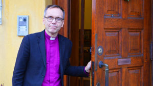 Stig på! På nyårsdagen är Biskopsgården öppen för besök. En man står utomhus och håller upp en ytterdörr.