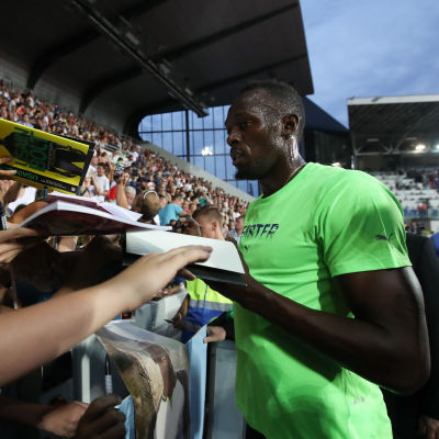 Usain Bolt delar ut autografer efter segerloppet.
