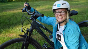 Jag är väldigt nöjd över att cykla med min hybridcykel med växlar. Malin Valtonen poserar vid en cykel med en vit cykelhjälm på huvudet.