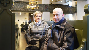 Ulla Juselius och Timo Kraufvelin skojar om att det snabbt kan bli för varmt att sitta med ytterkläderna på nu när jordvärmen kommit igång. En kvinna och en man sitter i kyrkbänken inuti Borgå domkyrka.