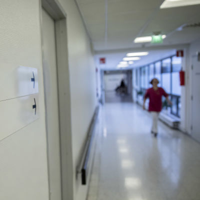 Tunnistamaton sairaanhoitaja käveleen sairaalan käytävällä. Etualalla tarkennettuna laboratorio ja röntgen kyltit seinässä.