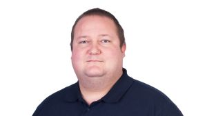 Tomson Holmlund kommer ursprungligen från Helsingfors, men stannade kvar i Ekenäs efter studietiden. En man med kort här och mörk tröja med korta ärmar, jeans och händerna i fickorna tittar allvarligt in i kameran.