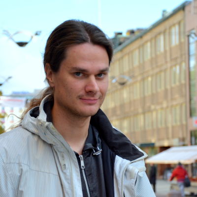 en man i grå jacka står vid gågatan i Åbo där människor går och cyklar omkring