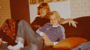 Leveästi hymyilevä Petteri Pykäläinen pikkupoikana sohvalla äitinsä kainalossa.