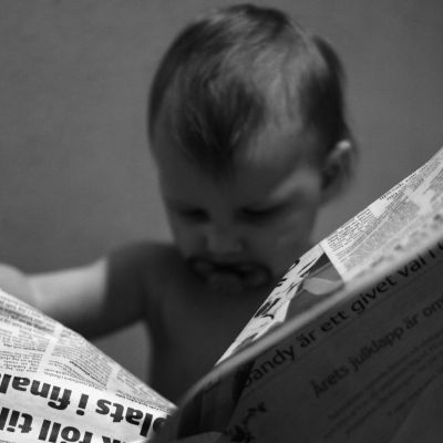 Barn läser tidning. Bilden är svartvit.