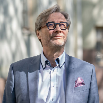 Markku Mäkijärvi tittar uppåt mot sidan. Solen skiner honom i ansiktet och han kisar lite.
