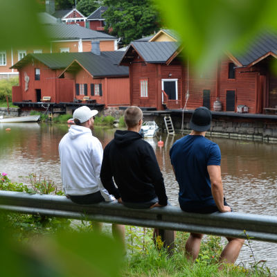 De tre pojkarna sitter med ryggen mot och tiitar ut över Borgå å och strandbodarna.