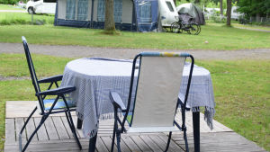Det här är uterummet hos Marina och Kalle som har sin plats i ett hörn längst in på campingområdet. ETt bord med duk och två stolar ute på en campingplats.