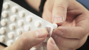 Rester av hormoner och p-piller finns också i avloppsslammet. Närbild på två händer som trycker ut ett piller ur en pillerkarta. Pillren är små och vita.