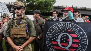 Qanon-protest i USA. På bilden syns militär samt en person som håller upp en flagga med rörelsens logo samt flera andra som protesterar.