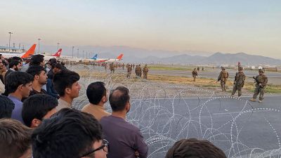 Folk står bakom taggtråd medan amerikanska soldater håller vakt på flygplatsen i Kabul.