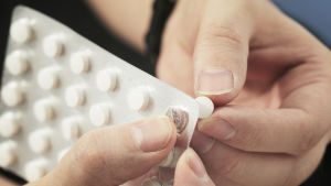 Närbild på två händer som trycker ut ett piller ur en pillerkarta. Pillren är små och vita.