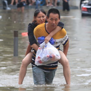 En man bär en kvinna på ryggen genom den översvämmade staden Zhengzhou.