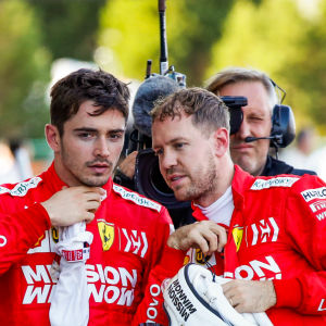 Leclerc och Vettel står bakom en Ferarribil och talar med varandra.