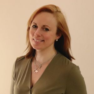 Anna Bertills tittar in i kameran och håller några papper och en penna i händerna.
