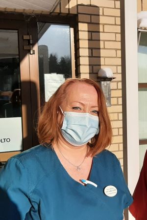 Hälsovårdaren Carola Silander-Lehtinen säger att det inte är möjligt att välja vilket vaccin som används under vaccinationerna. Två hälsovårdare med munskydd vid ingången till en hälsocentral, Carola Silander-Lehtinen i blå sköterskedräkt och Camilla Rautanen i röd sköterskedräkt.