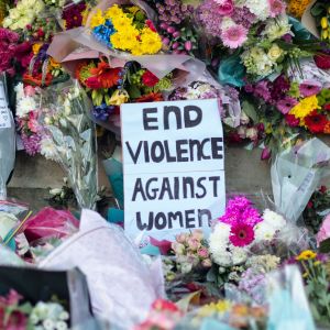 Plakat där det står "end violence against women" omgiven av blommor.