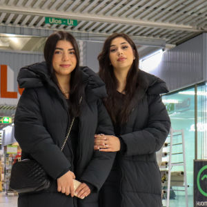 Två unga kvinnor står i armkrok i ett köpcenter. 
