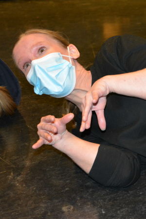 Lisa Taulio ligger som en nyfödd kattunge, då workshoppen hade teaterimprovisation. Lisa Taulio, en dam med svart tröja, jeans och ett ljusblått munskydd, ligger på en teaterscen med fingrarna utspärrade som en nyfödd kattunge.