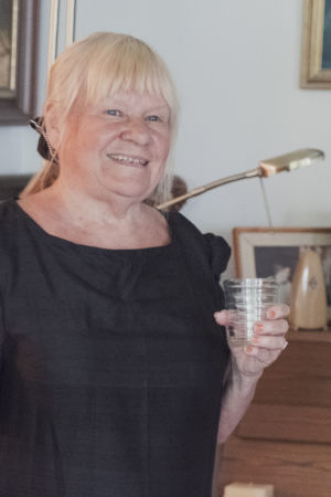 Maritta Pellava toivottaa meidät tervetulleeksi. Maritta Pellava pianonsa edessä vesilasi kädessään.