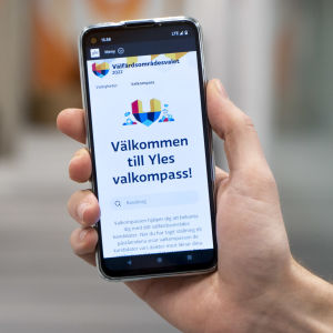 Närbild på mobiltelefon som visar upp startsidan för Svenska Yles valkompass med texten "Välkommen till Yles valkompass"