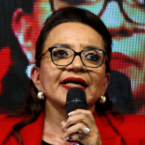 En kvinna i röd jacka håller tal.