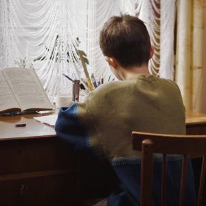 En pojke fotograferad bakifrån medan han sitter och jobbar vid ett skrivbord och läser.