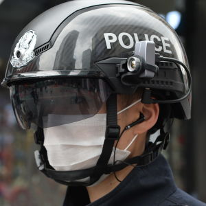 Två män i mörkblå polisuniform med hjälmar på huvudet med texten "POLICE". Hjälmarna har kameror och mörka visir.