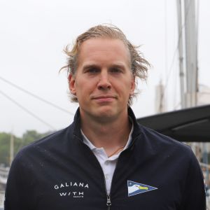 En man står på en brygga, i bakgrunden segelbåtar.