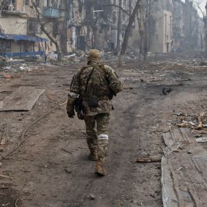 Sotilas kävelee kadulla selkä kameraan päin, taustalla tuhoutuneita rakennuksia.