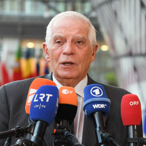 Josep Borrell med en rad mikrofoner framför sig och EU-flaggor samt många olika länders flaggor bakom sig.