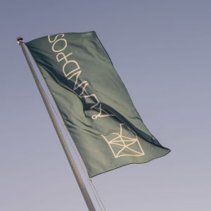 Tre flaggor med texten Åland post vajar i vinden mot en klar himmel.