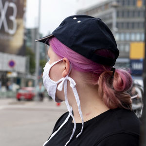 Nuori nainen lukee opinto-opasta kasvomaski naamallaan Helsingin keskustassa.