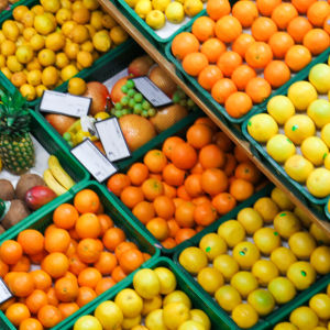 En person skuffar en kundvagn framför ett stort sortiment av bland annat citrusfrukter.