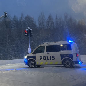 Polisbil spärrar av korsning med trafikljus. Snö på marken.