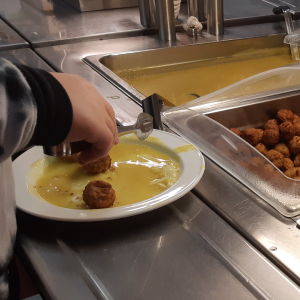 En skolelever tar köttbullar åt sig i en skolmatsal.