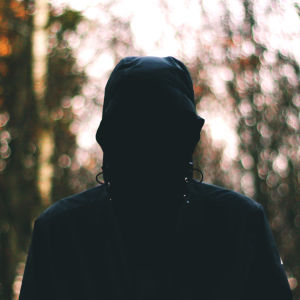 En man med dolt ansikte står i en skog.